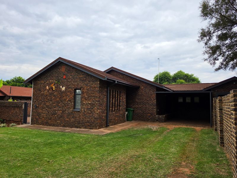 A rear view of a face brick house featuring a tiled roof, a covered carport, and a private garden area.
