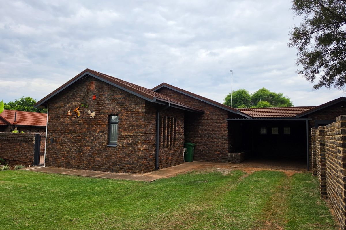 A rear view of a face brick house featuring a tiled roof, a covered carport, and a private garden area.