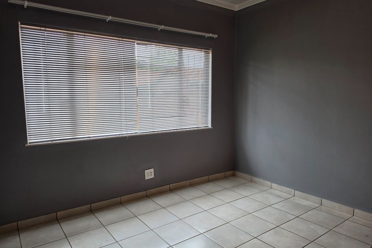 An empty bedroom featuring neutral tiled flooring, dark grey walls, and fitted venetian blinds, providing a clean and versatile space.