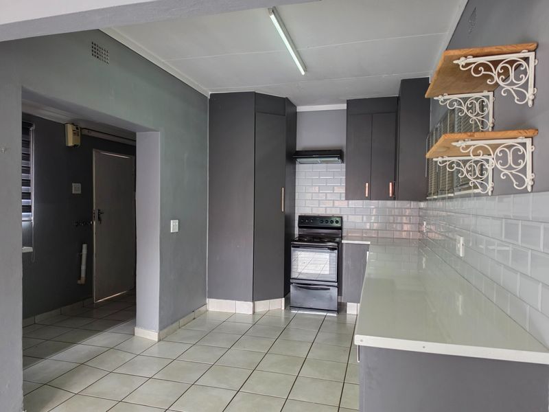 A functional kitchen featuring dark grey cabinetry, white subway tile backsplash, and tiled flooring, offering a clean and neutral space ready for personalization.