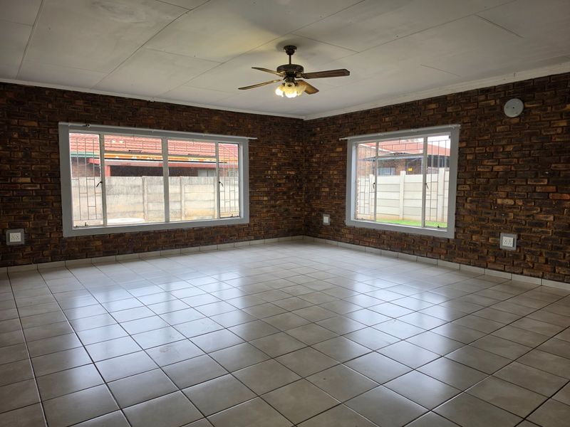 Spacious living area featuring exposed brick walls, ceramic tile flooring, and a ceiling fan, offering a blank canvas for interior design.
