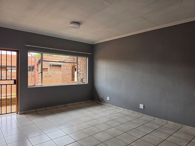 An empty living room featuring neutral tiled flooring, grey painted walls, and a security gate leading to the exterior.
