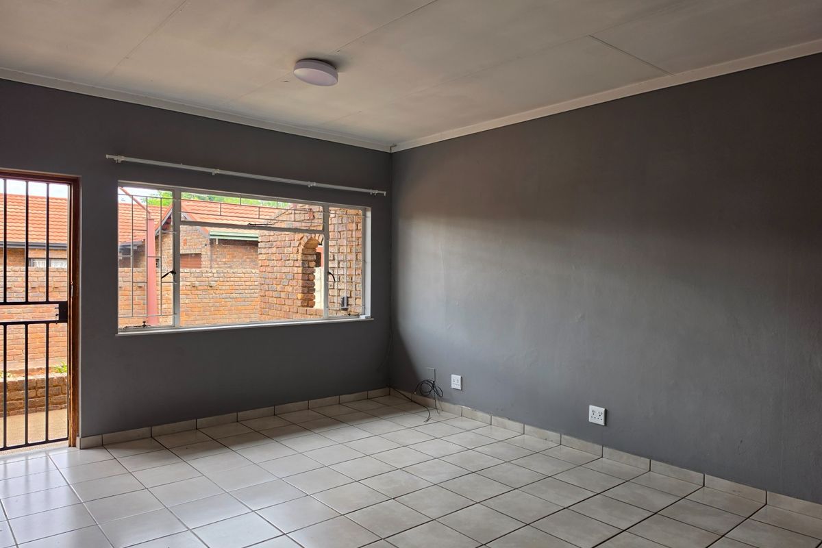 An empty living room featuring neutral tiled flooring, grey painted walls, and a security gate leading to the exterior.