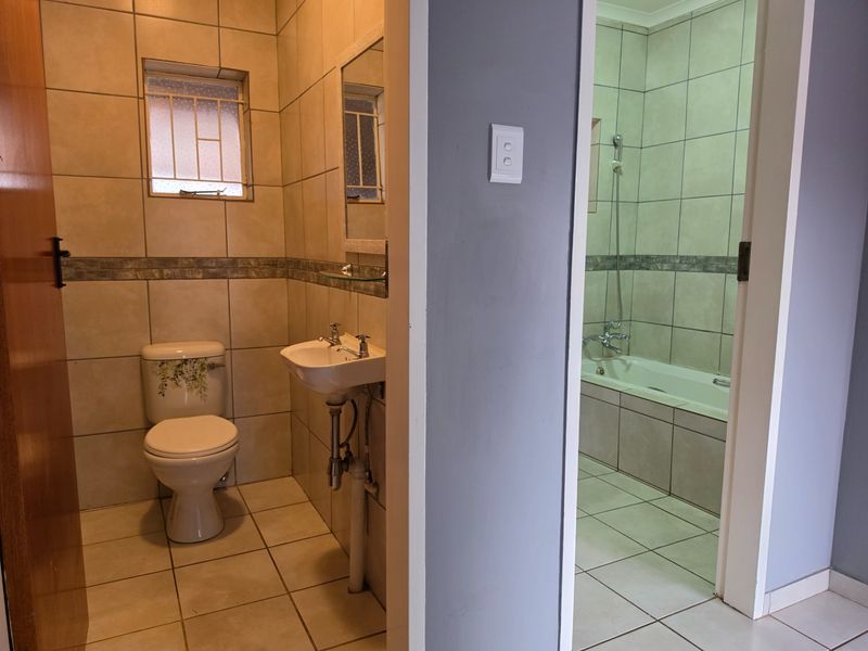 A functional bathroom featuring tiled walls and floors, a pedestal basin, toilet, and a separate bathtub area.