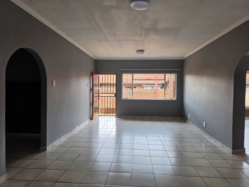 Spacious, empty living area featuring neutral grey walls, tiled flooring, and an arched entryway, providing a blank canvas for interior design.