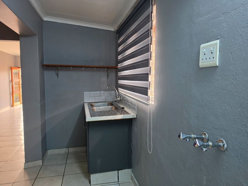 A functional laundry area featuring a stainless steel sink, tiled splashback, and dedicated plumbing connections for appliances, finished with neutral grey walls.