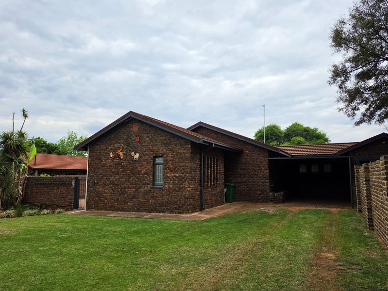 A single-story face brick house featuring a tiled roof, an integrated carport, and a well-maintained lawn in the front garden area.