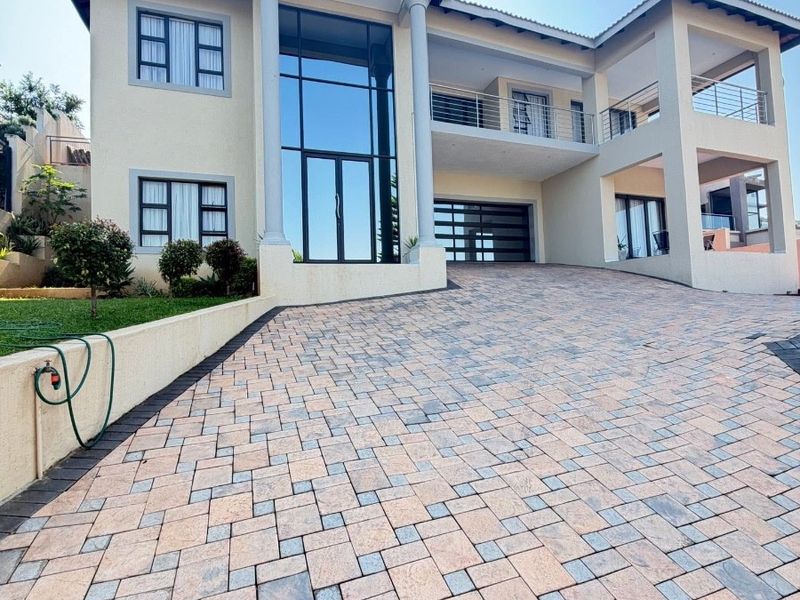 A modern multi-story apartment building featuring a large paved driveway, double garage, and prominent glass facade with balcony access.