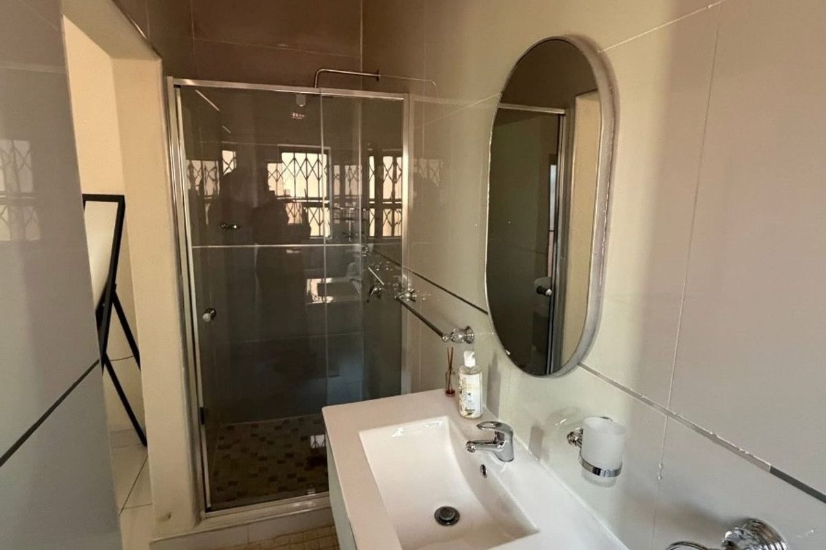 A modern bathroom featuring a glass-enclosed shower, a sleek vanity basin with a mixer tap, and neutral wall tiling.