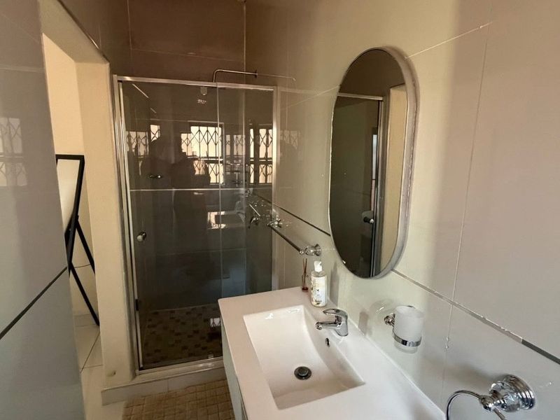 A modern bathroom featuring a glass-enclosed shower, a sleek vanity basin with a mixer tap, and neutral wall tiling.