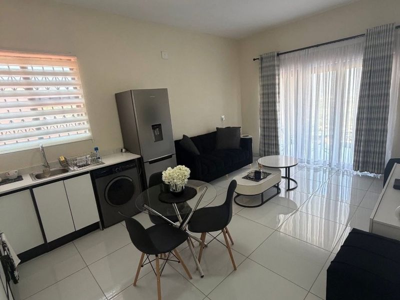 Modern open-plan living area featuring tiled floors, a compact kitchen with built-in cabinetry, and large sliding doors leading to an outdoor space.