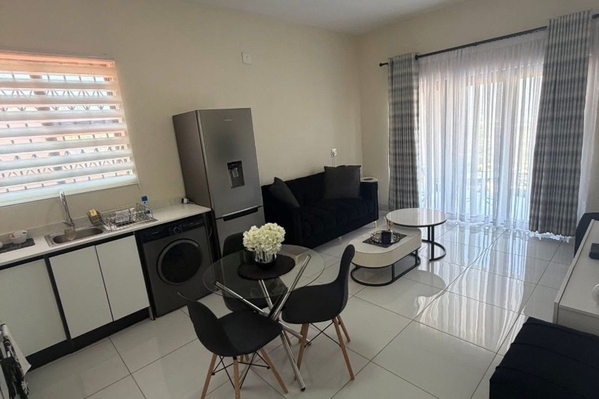 Modern open-plan living area featuring tiled floors, a compact kitchen with built-in cabinetry, and large sliding doors leading to an outdoor space.