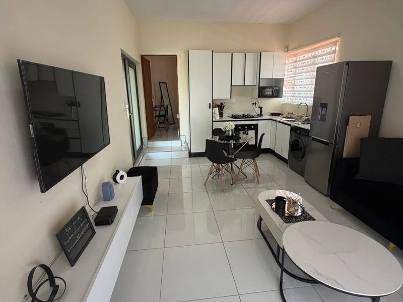 Modern open-plan living area featuring a compact kitchen with built-in cabinetry, integrated appliances, and sleek tiled flooring throughout the space.