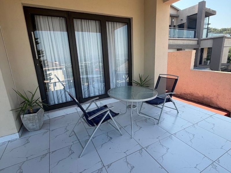 A covered balcony featuring large format marble-look floor tiles and sliding glass door access to the interior living space.