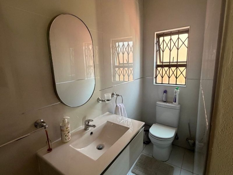 A modern, well-maintained bathroom featuring a wall-mounted vanity with a ceramic basin, tiled finishes, and secure window burglar bars.