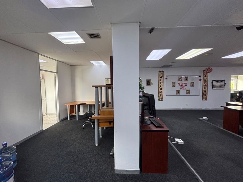 Open-plan office space featuring recessed lighting, carpeted flooring, and a central structural column, with an adjacent secondary room accessible via a glass door.
