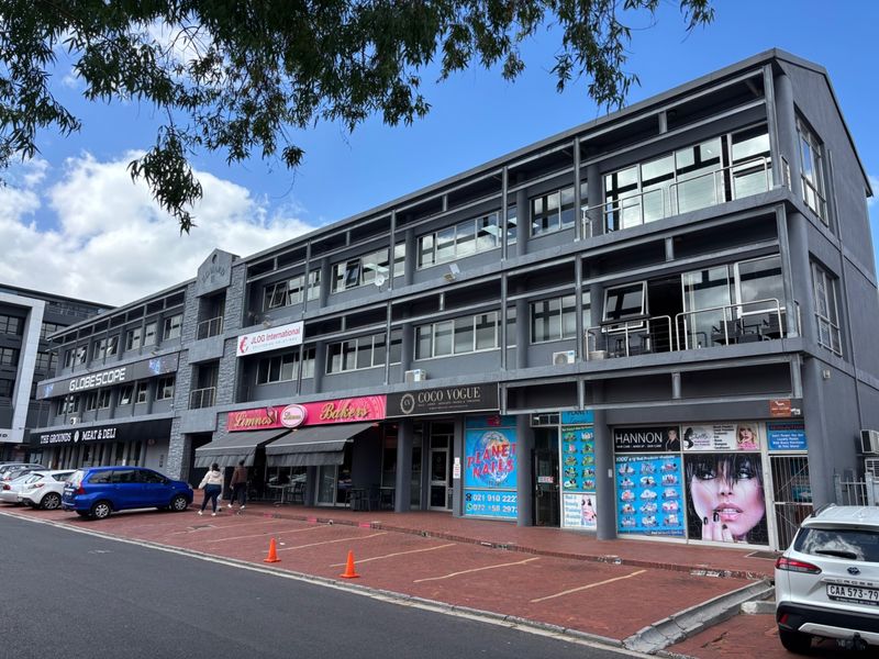 A multi-story commercial office building featuring a paved parking area, ground-floor retail storefronts, and upper-level office spaces with balconies.