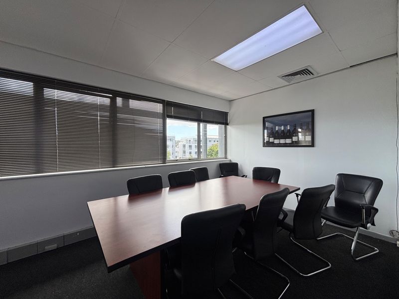 A professional office meeting room featuring large windows with venetian blinds, recessed ceiling lighting, and integrated air conditioning.