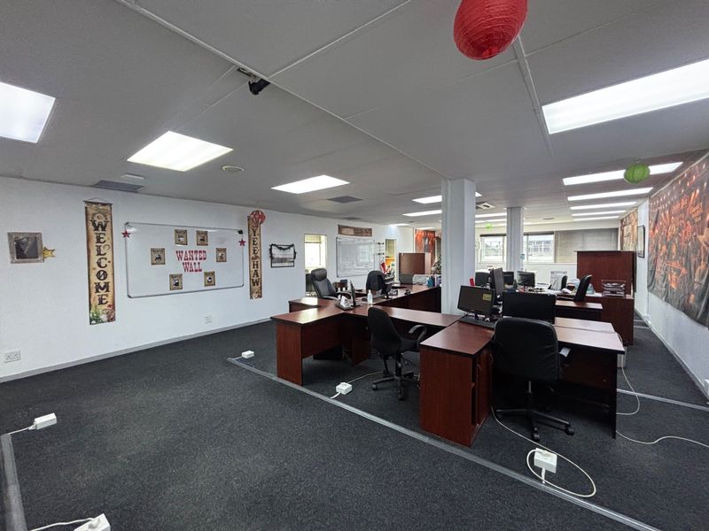 A spacious open-plan office area featuring suspended ceilings, recessed lighting, and carpeted flooring, providing a functional workspace environment.