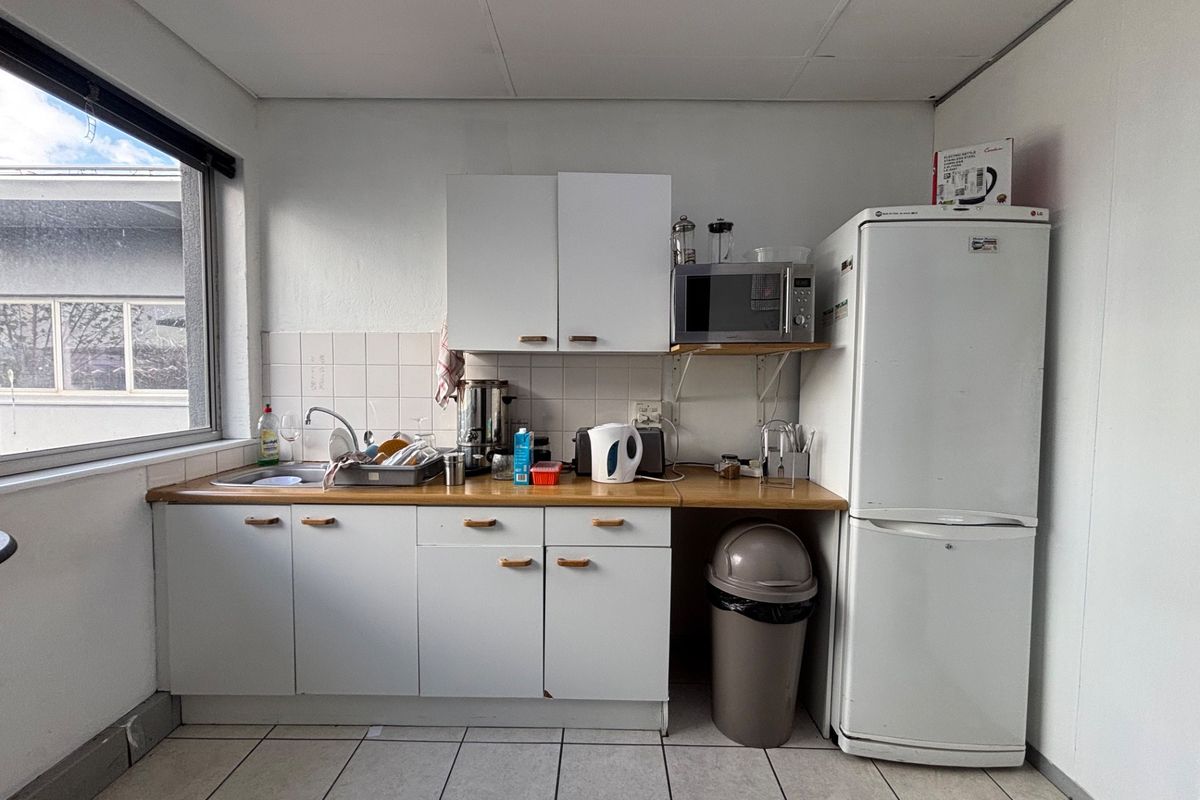 A compact office kitchenette featuring white cabinetry, a laminate countertop, tiled backsplash, and tiled flooring, providing essential utility space for staff.