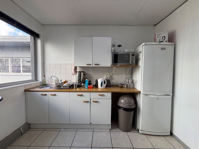 A compact office kitchenette featuring white cabinetry, a laminate countertop, tiled backsplash, and tiled flooring, providing essential utility space for staff.