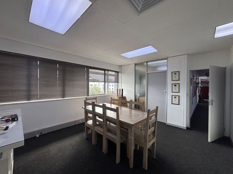 A functional office space featuring suspended ceilings, recessed lighting, carpeted flooring, and large windows with venetian blinds, providing a professional work environment.