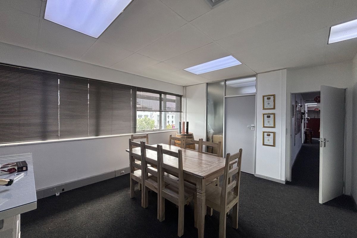 A functional office space featuring suspended ceilings, recessed lighting, carpeted flooring, and large windows with venetian blinds, providing a professional work environment.