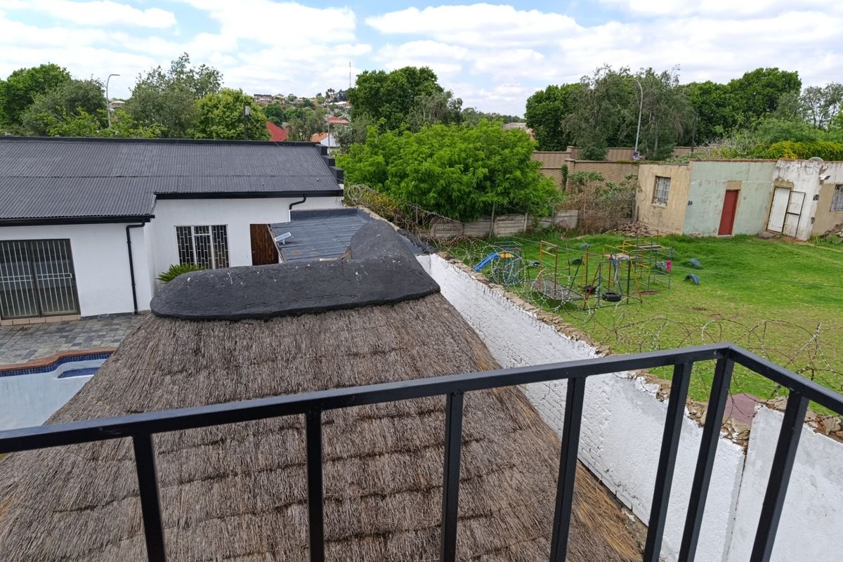 Elevated view overlooking a property with a thatched roof, metal roofing, and a perimeter wall with security fencing.