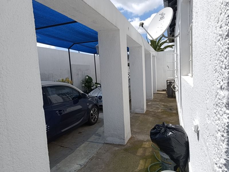 A covered outdoor patio area featuring concrete pillars and a shade cloth canopy, providing a functional space for vehicle parking or outdoor storage.