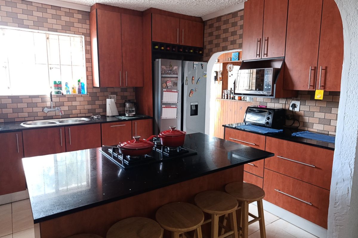 A functional kitchen featuring dark wood cabinetry, black granite countertops, a central island with a gas hob, and a tiled backsplash.