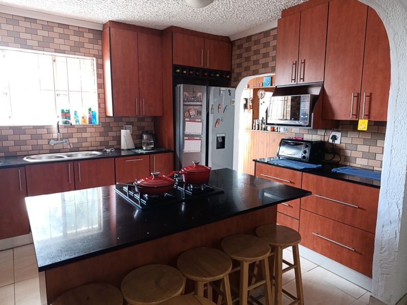 A functional kitchen featuring dark wood cabinetry, black granite countertops, a central island with a gas hob, and a tiled backsplash.
