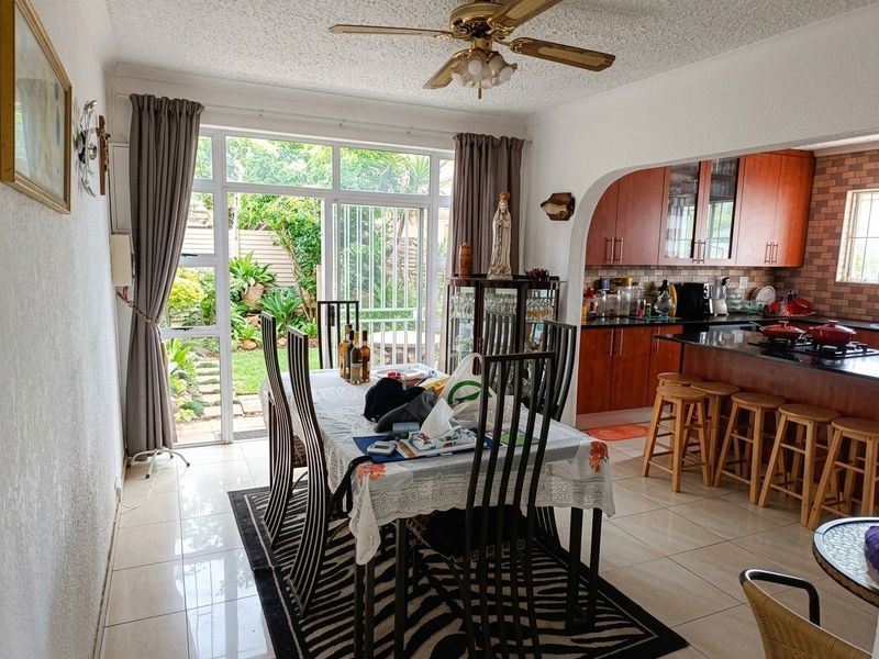 Open-plan dining and kitchen area featuring tiled floors, granite countertops, built-in cabinetry, and direct access to the garden through sliding glass doors.