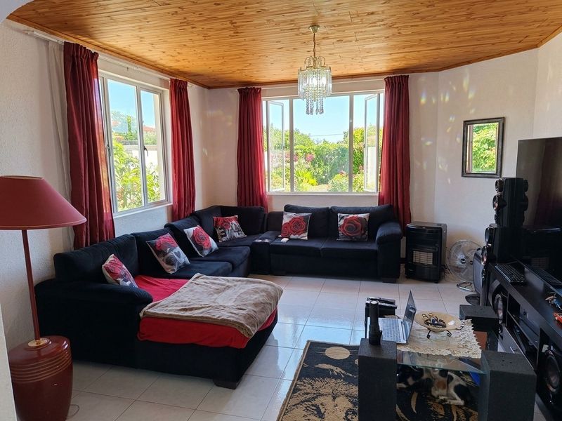 A spacious living room featuring a warm timber tongue and groove ceiling, tiled flooring, and large windows that provide ample natural light.