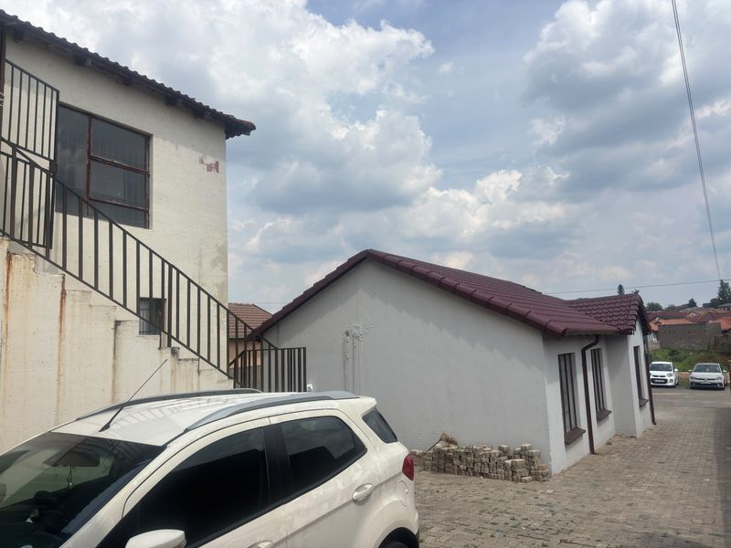 Rear exterior view of the property featuring a paved driveway, metal staircase, and tiled roof structures.