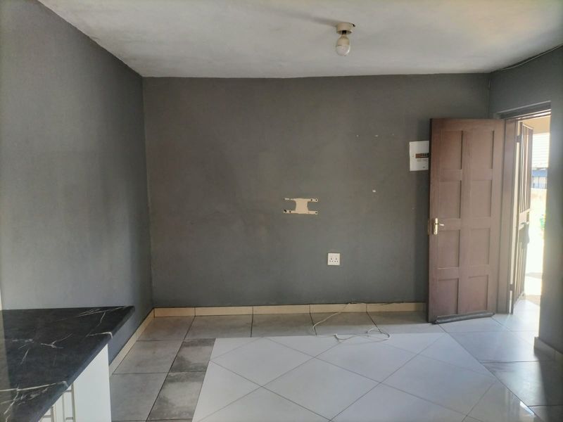 An open-plan living area featuring tiled flooring, a kitchen countertop, and direct access to an exterior entrance.
