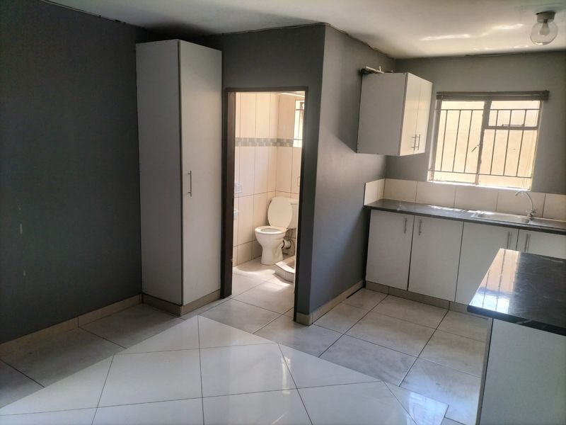 Open plan kitchen area featuring built-in cabinetry and tiled flooring, with an adjacent bathroom containing a toilet.