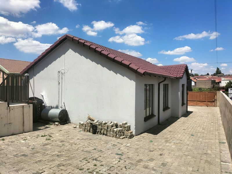Rear view of the property featuring a tiled roof, paved driveway, and perimeter boundary walling.