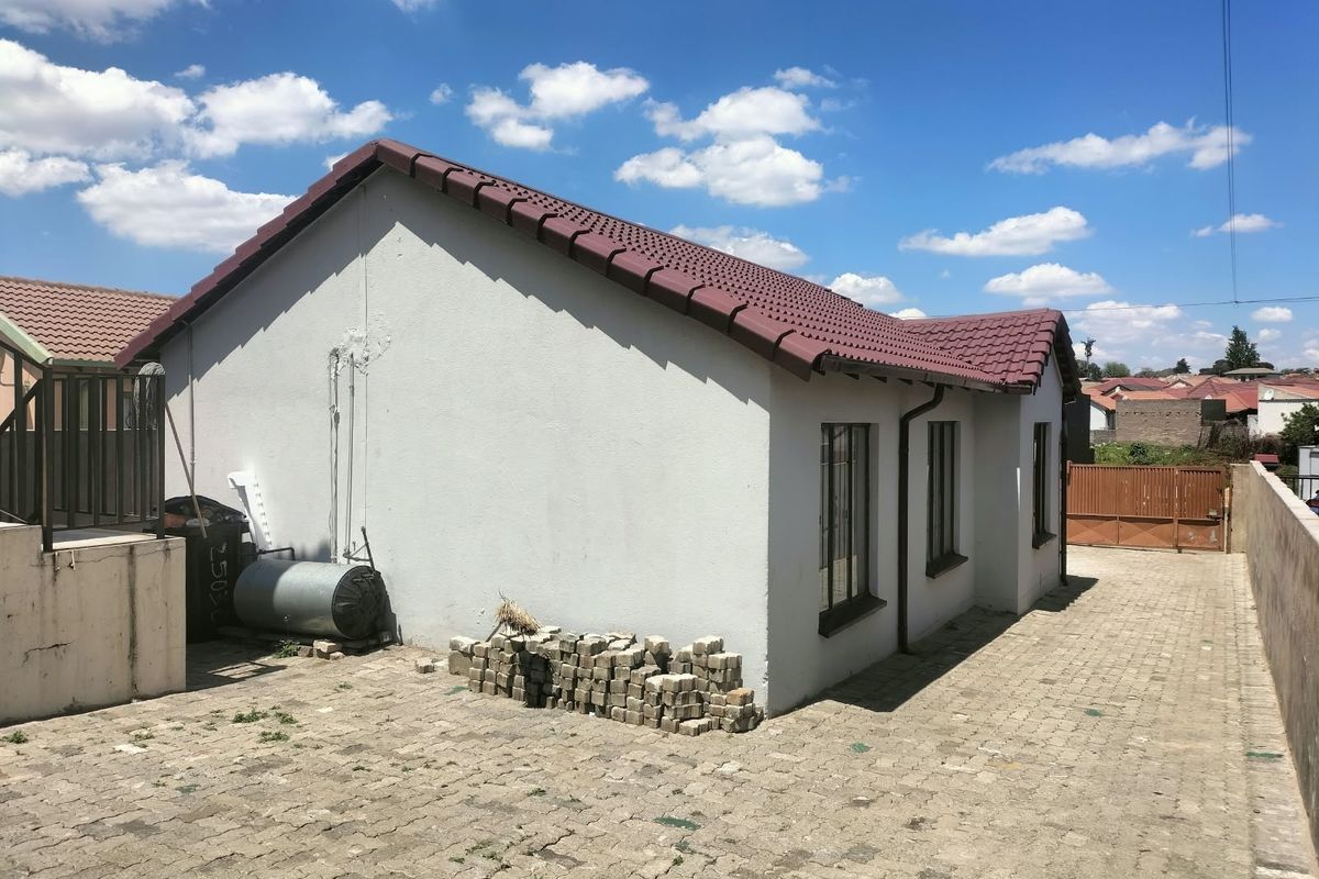 Rear view of the property featuring a tiled roof, paved driveway, and perimeter boundary walling.