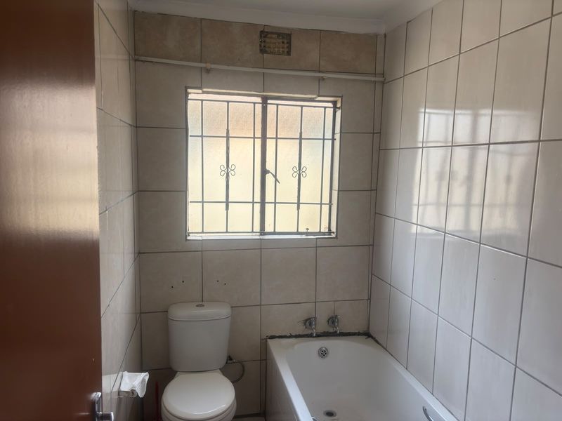 A functional bathroom featuring a built-in bathtub, toilet, and tiled walls. The space is ready for renovation to update the dated finishes.