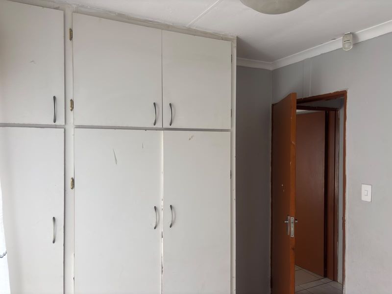 A bedroom featuring built-in cupboards and a standard internal door, showing signs of wear on the cabinetry and door frame.