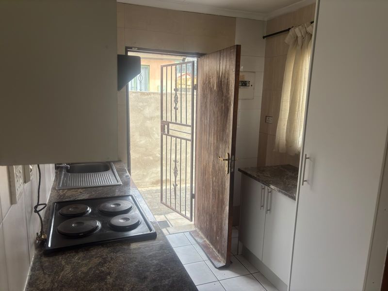 Compact kitchen featuring built-in cabinetry, laminate countertops, an electric hob, and direct access to the exterior via a security gate.
