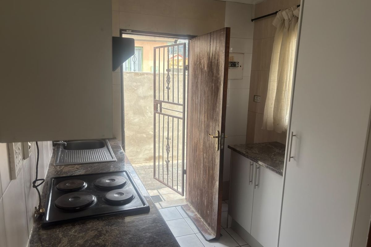 Compact kitchen featuring built-in cabinetry, laminate countertops, an electric hob, and direct access to the exterior via a security gate.