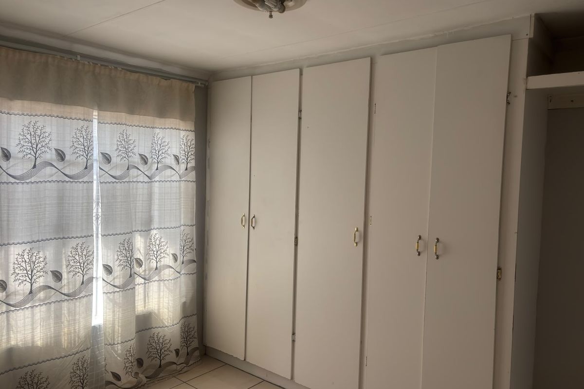 A bedroom featuring built-in cupboards and tiled flooring, offering a functional space ready for personalization.