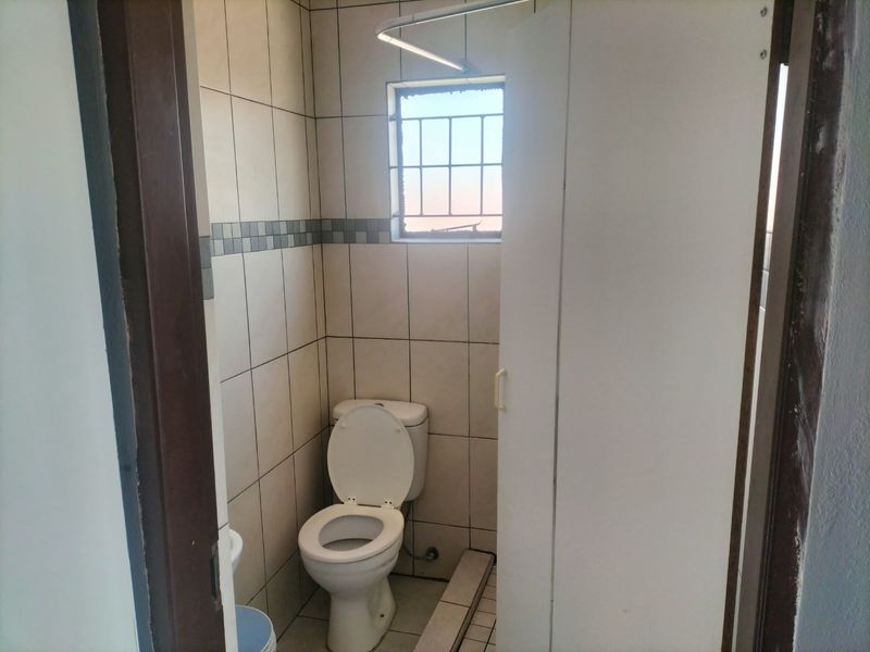 A compact bathroom featuring tiled walls, a standard toilet, and a window with security bars.
