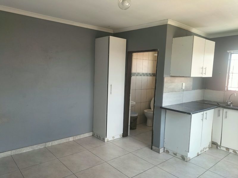 Open plan kitchen area featuring tiled flooring, built-in cabinetry, and a laminate countertop, with an adjacent bathroom entrance.