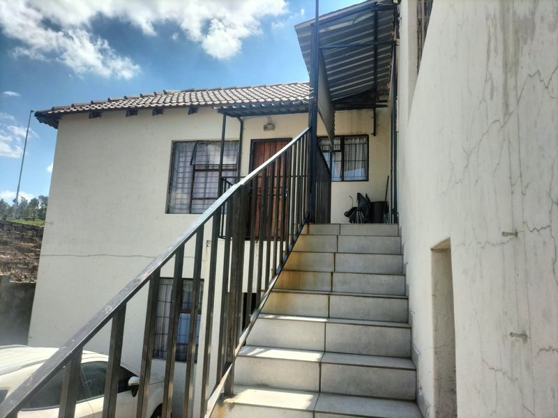 Exterior view of a cottage featuring an external tiled staircase with metal balustrade, security bars on windows, and a metal awning over the entrance.