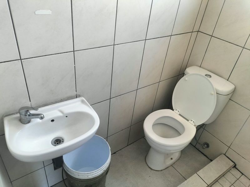 A compact bathroom featuring a wall-mounted basin and ceramic toilet with full-height wall tiling, requiring cosmetic updates to improve its overall condition.