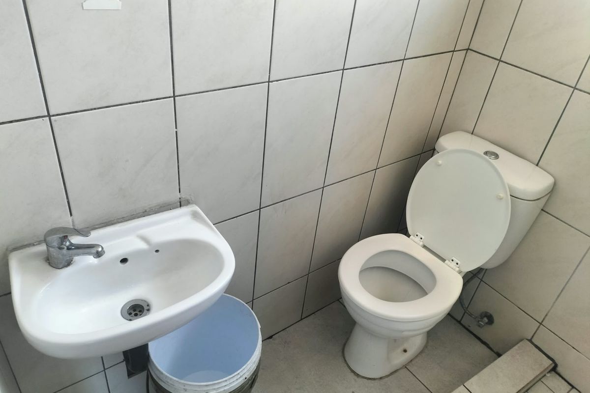 A compact bathroom featuring a wall-mounted basin and ceramic toilet with full-height wall tiling, requiring cosmetic updates to improve its overall condition.