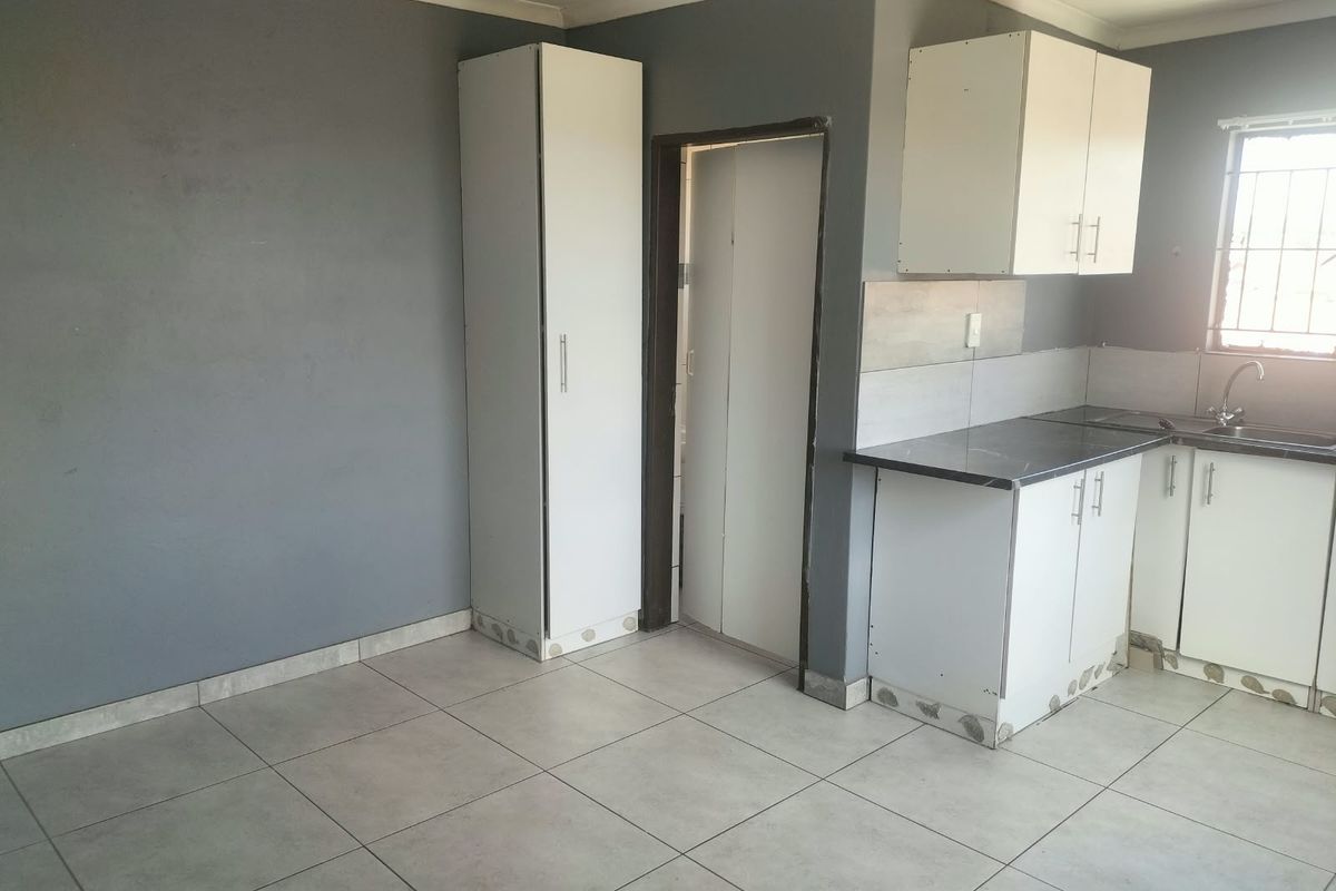 A compact kitchen featuring white cabinetry, dark countertops, tiled flooring, and grey walls, offering a functional space ready for personalization.