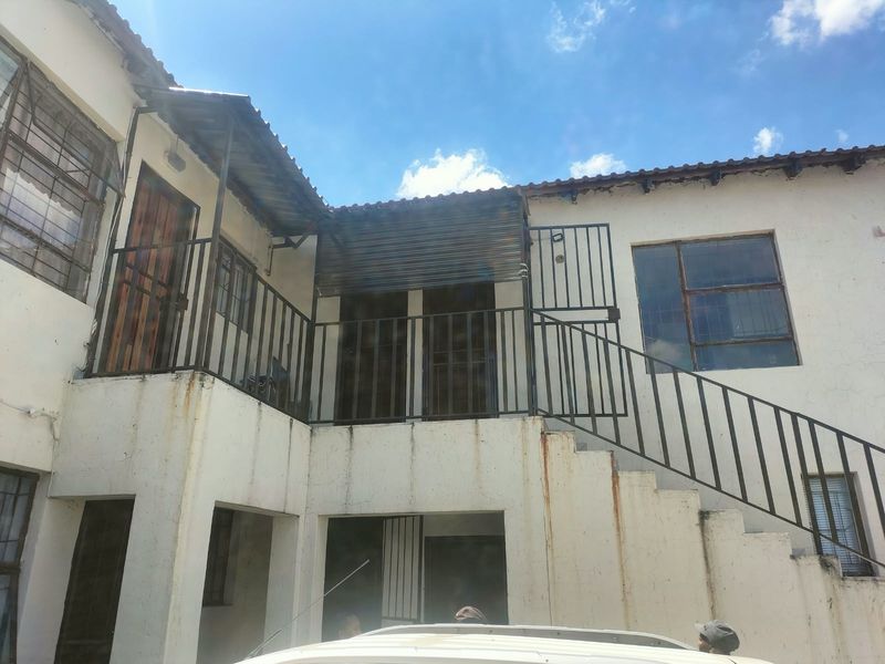 Rear exterior view of the cottage featuring a metal staircase, security gates, and window bars, showing signs of weathering and rust staining on the walls.